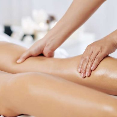 Hands of massage therapist massaging legs of young woman in spa salon
